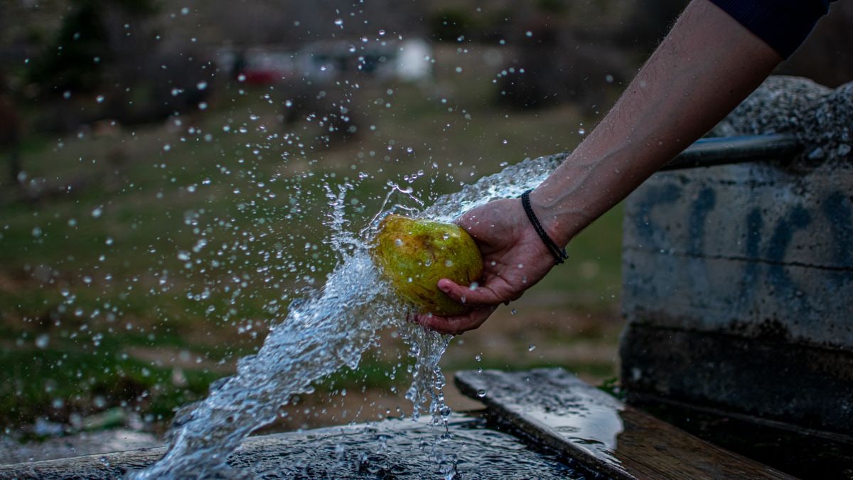 Person washing a pear under a running tap, capturing water splashing outdoors in Komnina, Greece.